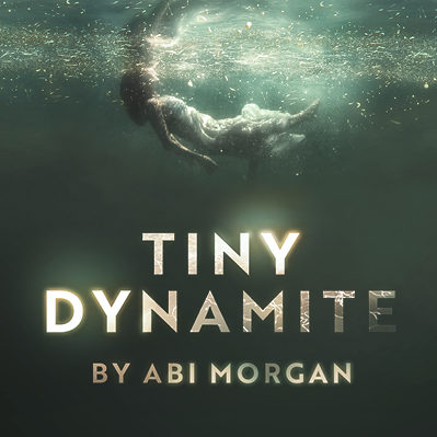 A woman wearing a white dress with lots of material floats just under the surface of dark green water. Specks of light dance close to the surface. Below her the title reads "TINY DYNAMITE BY ABI MORGAN" with glowing block letters.