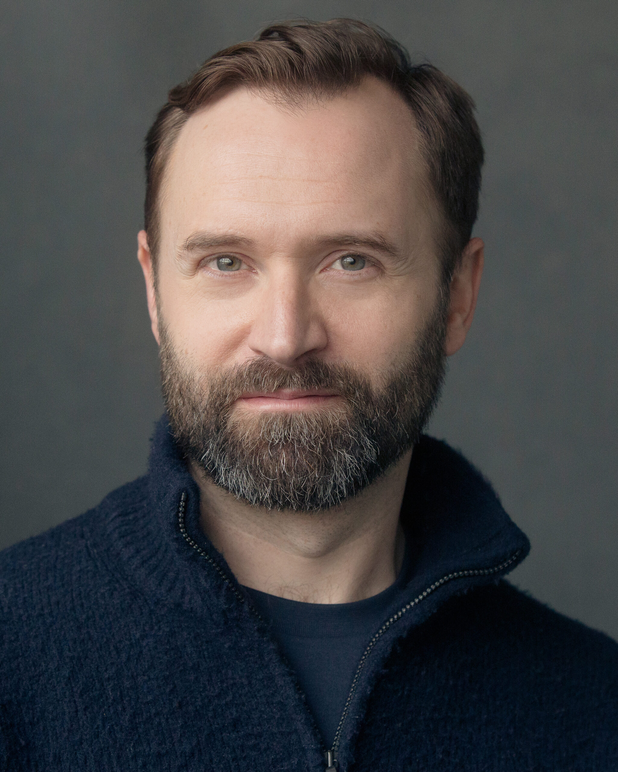 Headshot of Alastair Brookshaw. A man with brown hair and brown and grey beard. He is wearing a navy half-zip jumper with navy t-shirt underneath.