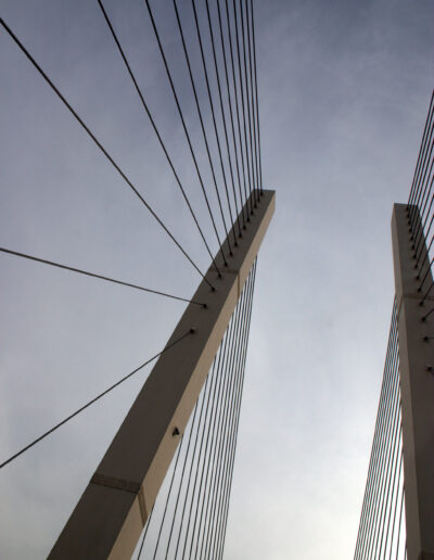 Tall white pillars with lots of cables criss-crossing downwards to form triangles. The sky is cloudy and the light is dimming.