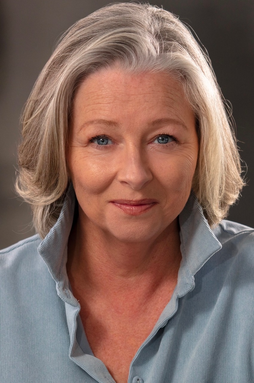 Headshot of Sarah Ingram, an older woman with white hair in a bob and blue eyes. She is wearing a blue textured shirt with collar up.