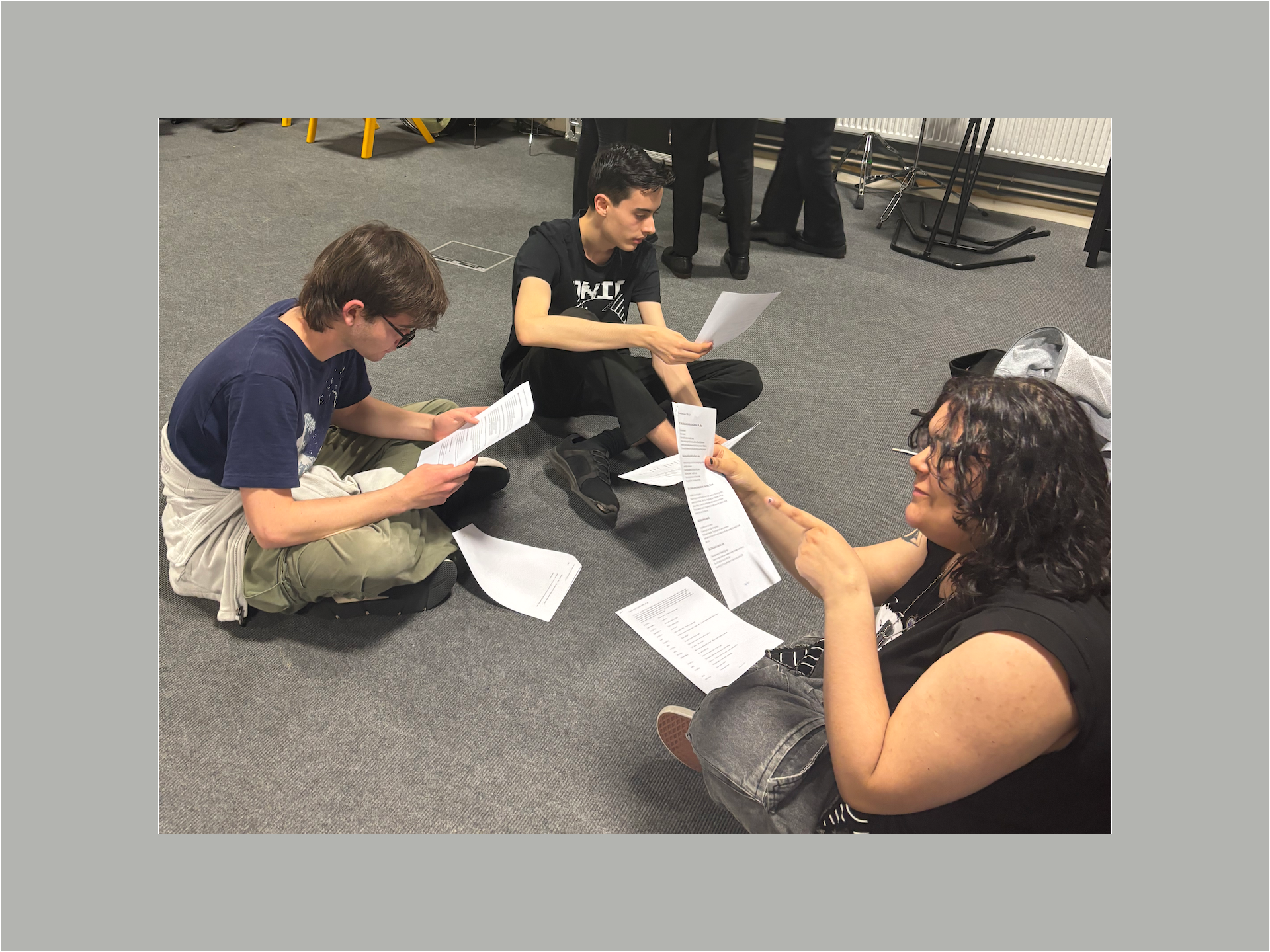 Three pupils sit on the floor of a rehearsal room reading scripts.
