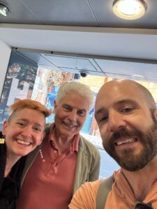 A selfie of P Burton-Morgan, Ian Grant & Gavin Dent in front of a train station concourse shop.